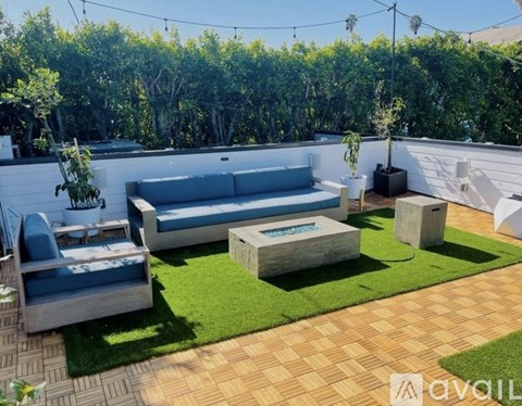 A patio with a couch, table, and chairs is surrounded by a grassy area and trees.