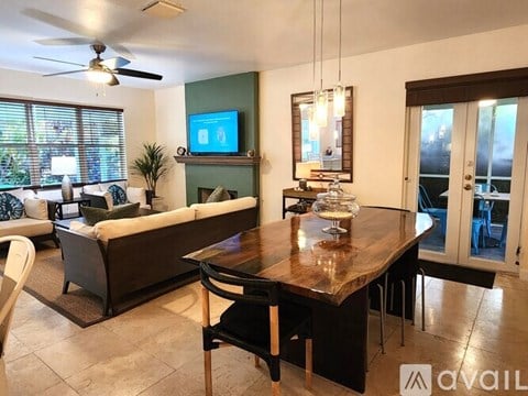 A modern living room with a television on the wall and a dining table in the center.