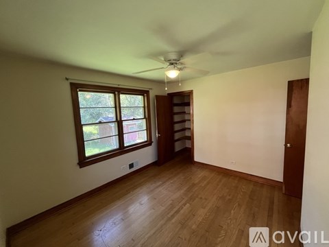 A room with wooden floors and a window with a view of trees and a house.