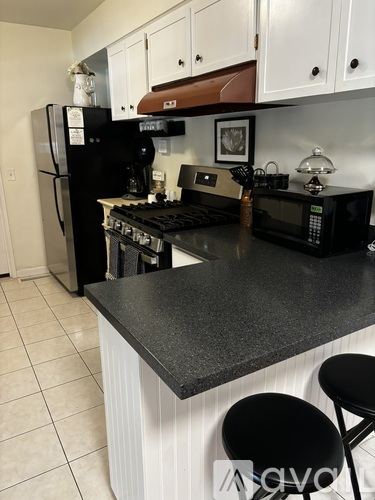 A black fridge and microwave in a kitchen with white cabinets.