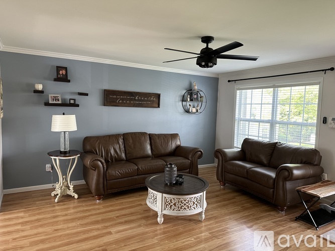 A living room with brown leather couches and a ceiling fan.