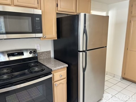 A black refrigerator stands next to a stove in a kitchen.