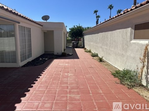 A red brick pathway leads to a white building with a satellite dish on top.