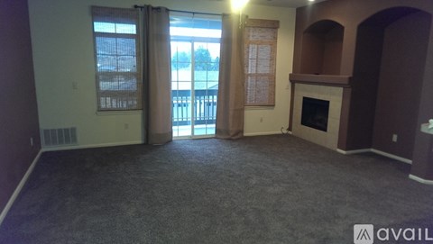 A room with a fireplace and a large window with a view of a fence and trees.
