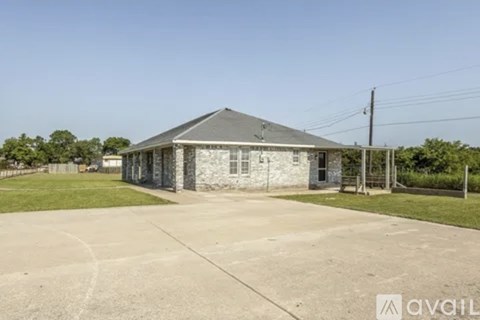 A house with a grey roof and a white wall is surrounded by a concrete driveway.