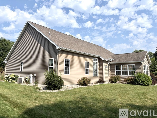 A house with a brown siding and a grey roof is surrounded by green grass.