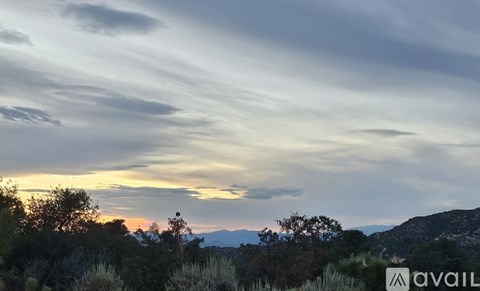 A landscape with trees and mountains under a cloudy sky at sunset.