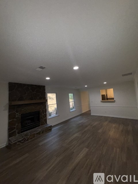 A spacious room with a stone fireplace and wooden flooring.