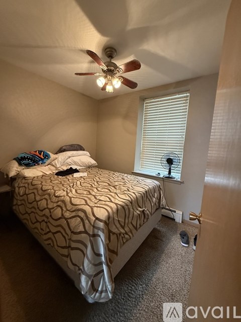 A bedroom with a bed, a ceiling fan, and a window with blinds.