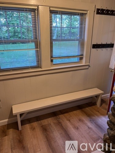 A white bench sits in front of a window with blinds.