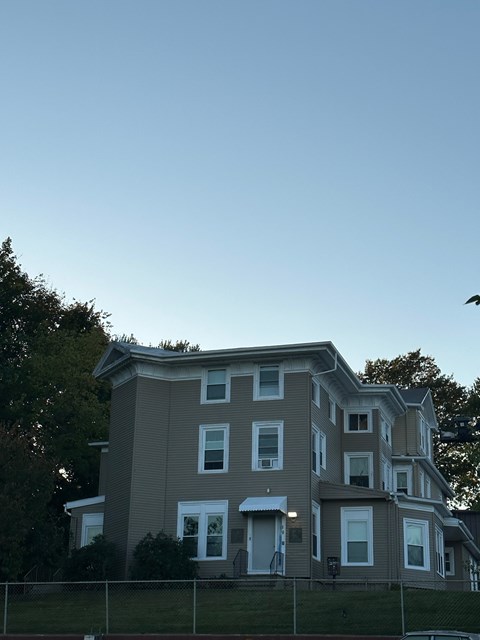 A large house with a grey and white exterior and a fence in front.