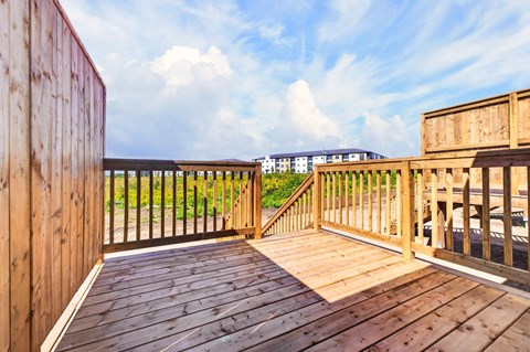 A wooden deck with a metal railing and a building in the background.