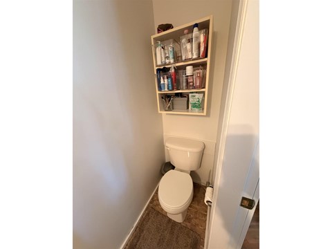 A white toilet in a small bathroom with a shelf above it.