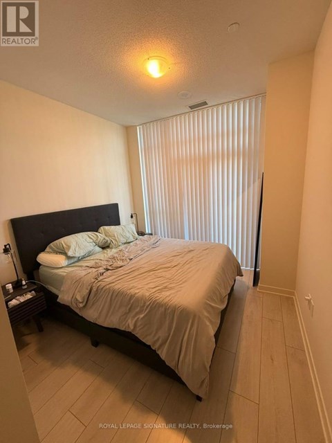 A bedroom with a bed, nightstand, and window with blinds.