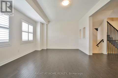 A spacious room with wooden floors and a staircase on the right side.