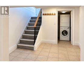 A hallway with a staircase and a washing machine in the doorway.