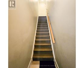A staircase with a wooden handrail and a black mat at the bottom.