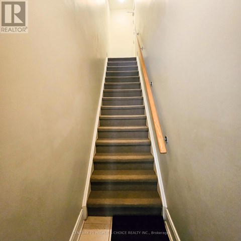 A staircase with a wooden handrail and a black mat at the bottom.