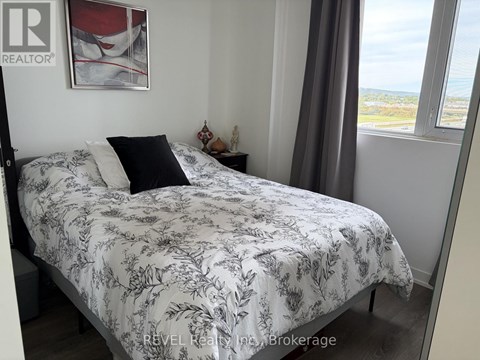 A bed with a floral patterned comforter is in a room with a window showing a view of the outdoors.