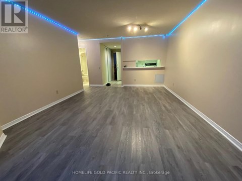A spacious room with wooden flooring and a hallway leading to another room.