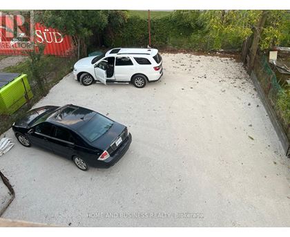 Two cars are parked in a gravel lot.