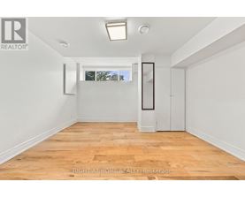 A room with wooden flooring and white walls, with a window showing trees outside.