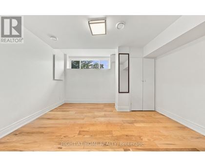 A room with wooden flooring and white walls, with a window showing trees outside.