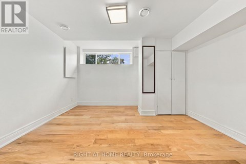 A room with wooden flooring and white walls, with a window showing trees outside.