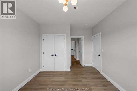 A spacious room with white walls and wooden flooring, featuring a row of white doors.