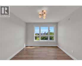 A well-lit, empty room with a large window and wooden flooring.