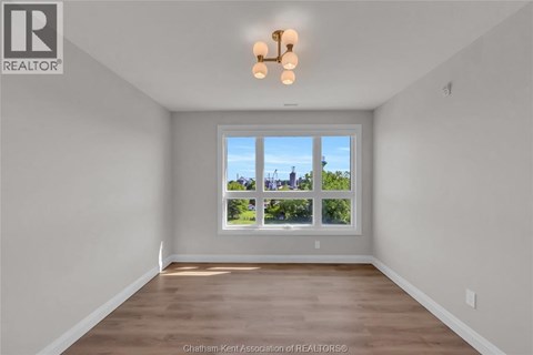 A well-lit, empty room with a large window and wooden flooring.