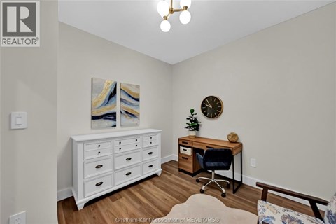A room with a white dresser, a desk with a chair, and a painting on the wall.