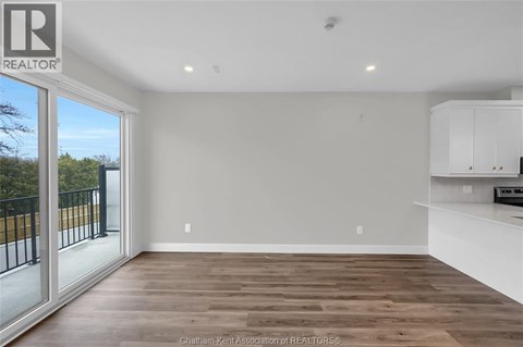 A spacious room with wooden flooring and white walls, part of a real estate listing.