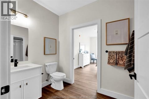 A white bathroom with wood floors and a white toilet.