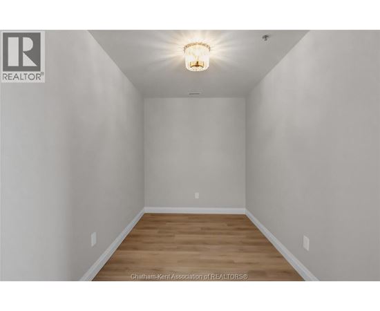 A white room with a light on the ceiling and wooden flooring.