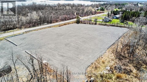 A large, empty parking lot sits in the foreground of a rural landscape.
