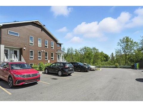 A red car is parked in a parking lot in front of a brown building.
