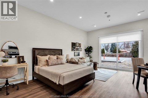 A bedroom with a large bed, a desk with a chair, and a window with a view of a backyard.