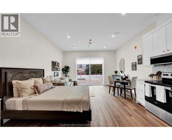 A well-lit bedroom with a large bed and a kitchen area with a stove and sink.