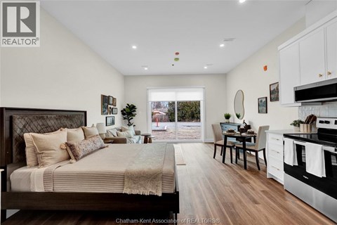 A well-lit bedroom with a large bed and a kitchen area with a stove and sink.