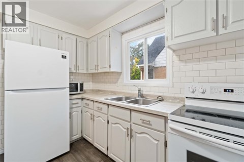 A white refrigerator stands in a kitchen with white cabinets and a white stove.