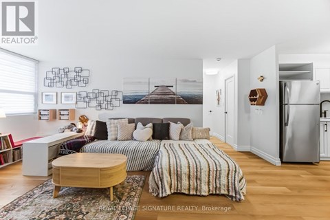 A well-lit bedroom with a large bed and a refrigerator in the corner.