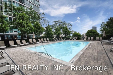 A swimming pool surrounded by lounge chairs and trees with a building in the background.
