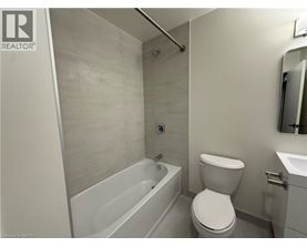 A white toilet is in a bathroom with a white tub and sink.