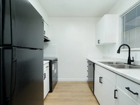 A black refrigerator is in a kitchen with white cabinets.