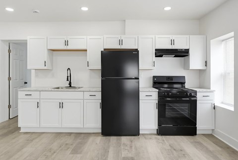 A black refrigerator stands in a kitchen with white cabinets and a black stove.