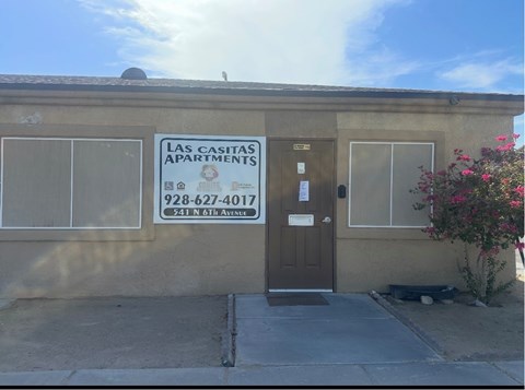The image shows the front of a building with a sign that reads "Las Casitas Apartments" and a phone number.