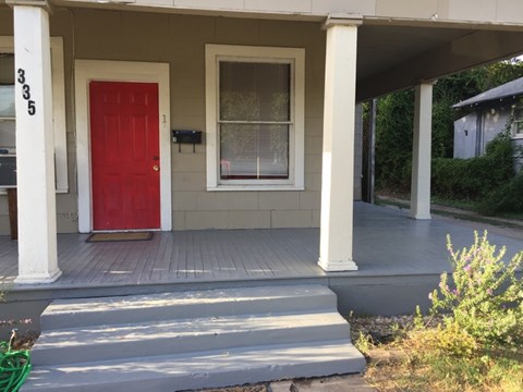 A red door is on the left side of a house with a porch.