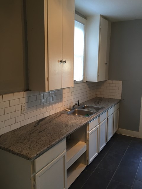 A kitchen with a granite counter top and white cabinets.