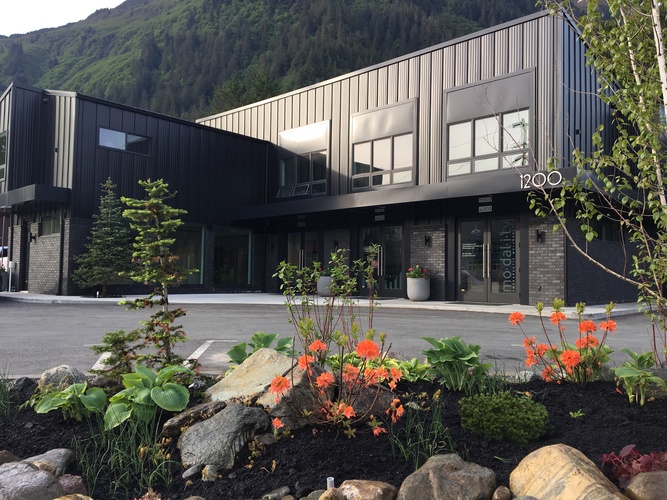 A modern building with a black and grey exterior and a garden in front.